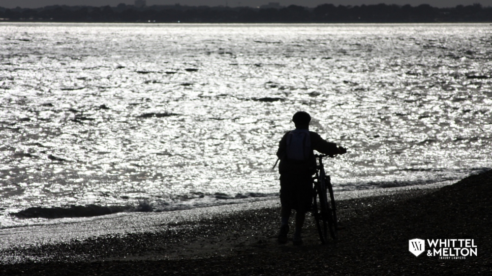 Persona caminando junto a una bicicleta al atardecer en la playa, con el logotipo de Whittel & Melton, abogados de lesiones personales en Florida.