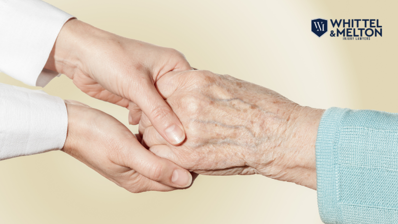 Manos de una persona mayor siendo sostenidas con cuidado por un cuidador, simbolizando apoyo y atención en un asilo o centro de cuidados para ancianos. Con el logo de Whittel & Melton.